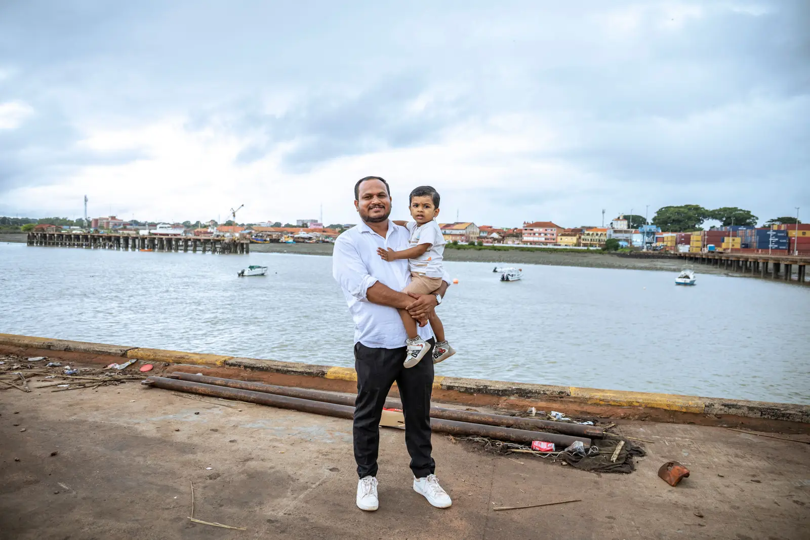 The director of Bafata Agri Resources holding his son on the Bissau waterfront, with the port and the estuary behind them.