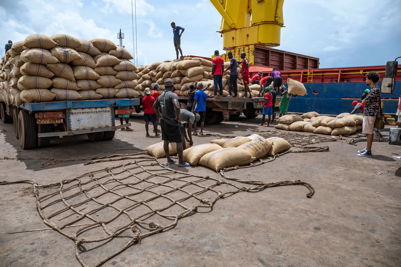 A loaded trailer at the quay in Bissau being unloaded by hand, with a cargo net laid out on the concrete ready for lifting.