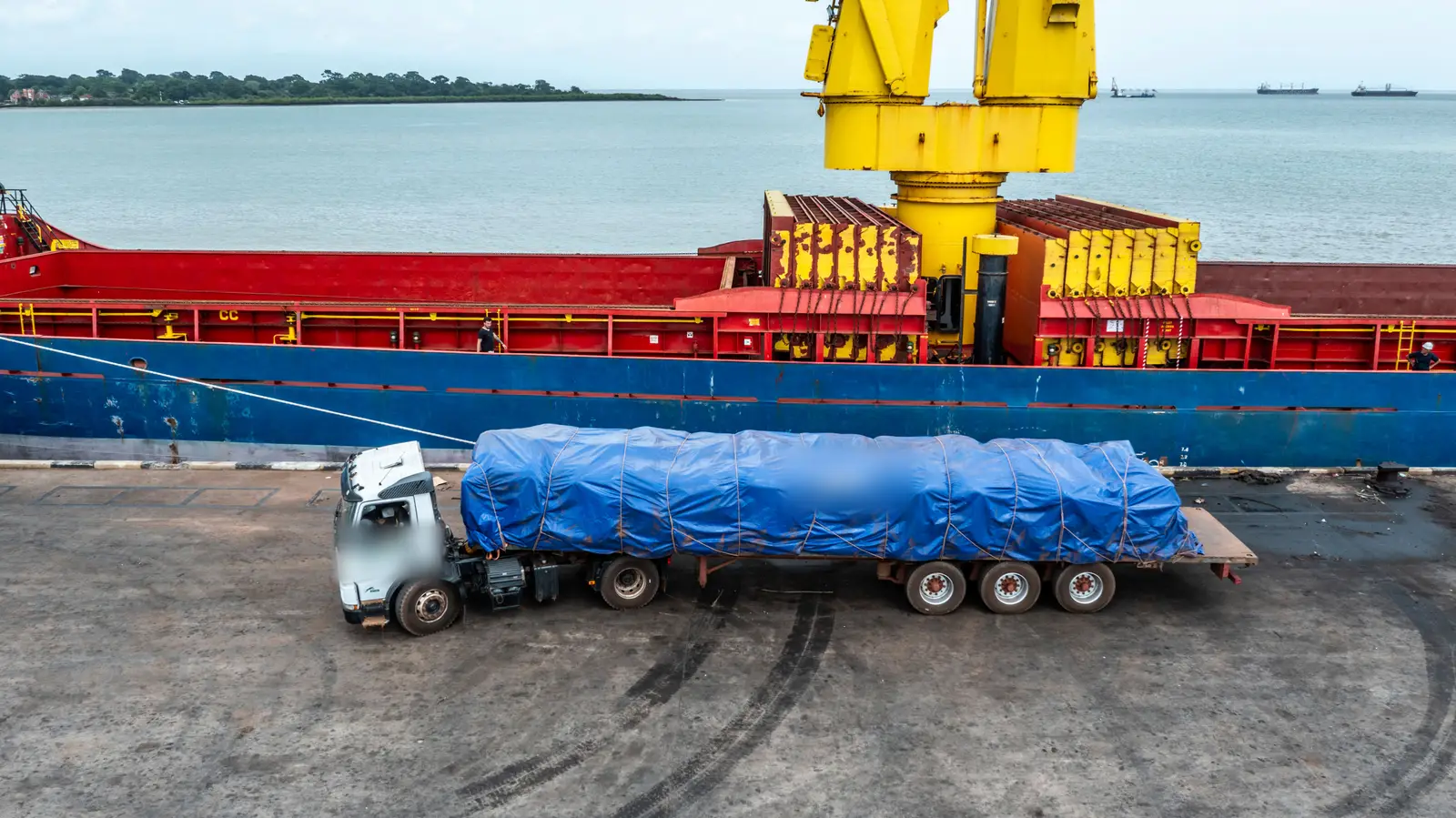 A sheeted trailer standing on the quay directly alongside the hull of the vessel it will be loaded into.